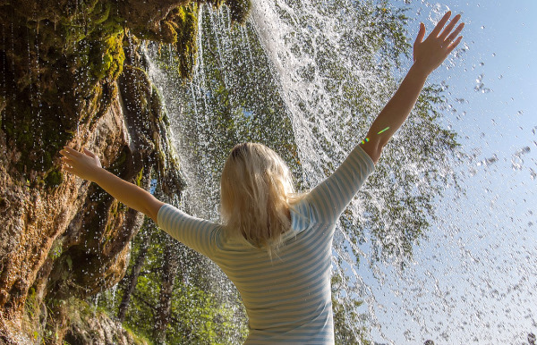 femme de dos sous une petite cascade recevant une pluie de bienfaits